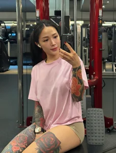 Janejaneey в спортзале, демонстрирующая татуировки на руке и ноге