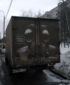 Фотография татуировки на кузове фургона: гигантское лицо с глазами и надписью 'Всё в пределах нормы'.