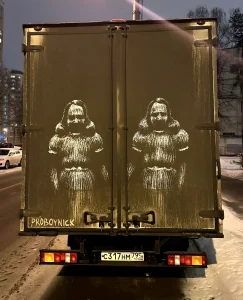 Фотография татуировки на задней двери фургона, изображающей два черепа в кокошниках, выполненной в технике трафарета.