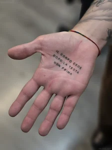 Фото татуировки на ладони: черная надпись 'Il corpo cede dopo la testa, non prima' на открытой руке мужчины.