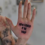 Черно-белая татуировка на ладони с фразой 'HOW COULD IT BE YOU?', минималистичный шрифт, вид сверху