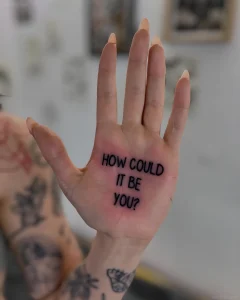 Черно-белая татуировка на ладони с фразой 'HOW COULD IT BE YOU?', минималистичный шрифт, вид сверху