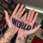 Черно-белая татуировка надписью 'WORLD' на раскрытых ладонях, вид сверху, с частично забитыми рукавами.