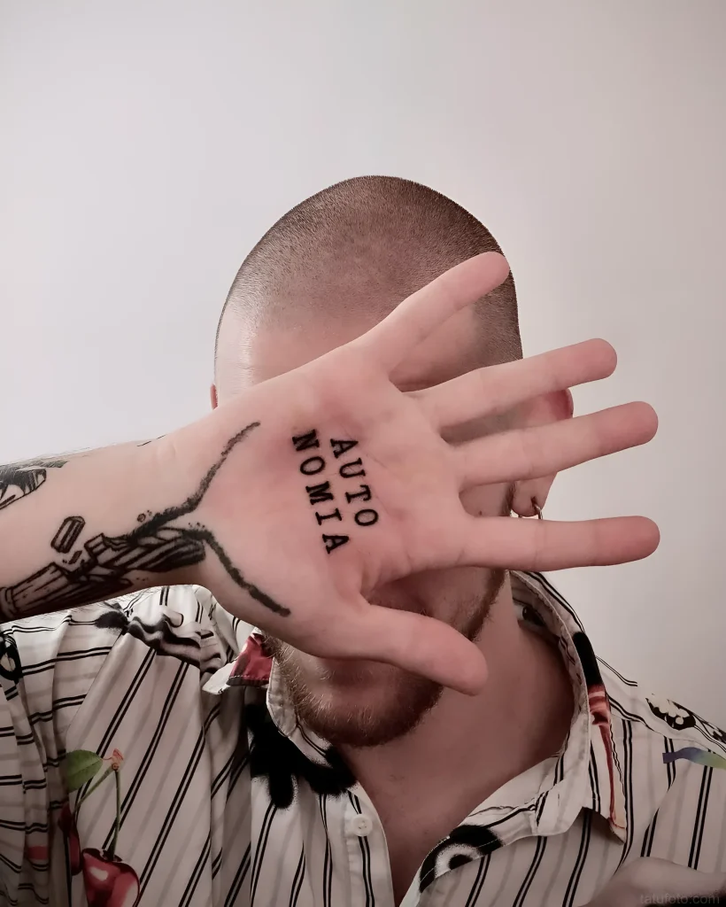 男人手掌上的黑白纹身,写着“Autonomia”字样,并带有象征独立和自由的猫爪图案。