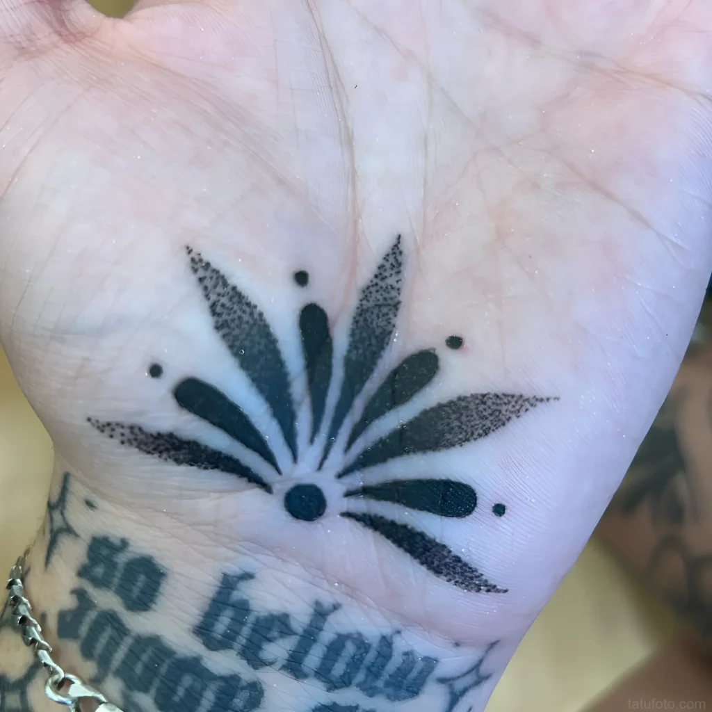 手掌上的黑白点画风格纹身,描绘了一朵风格化的花或太阳,边缘有点状图案。