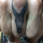 Фотография татуировки на пальце: стилизованный череп козла в технике blackwork, выполненный с акцентом на графичность и контраст.