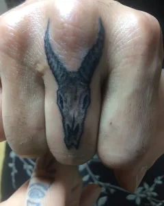 Фотография татуировки на пальце: стилизованный череп козла в технике blackwork, выполненный с акцентом на графичность и контраст.