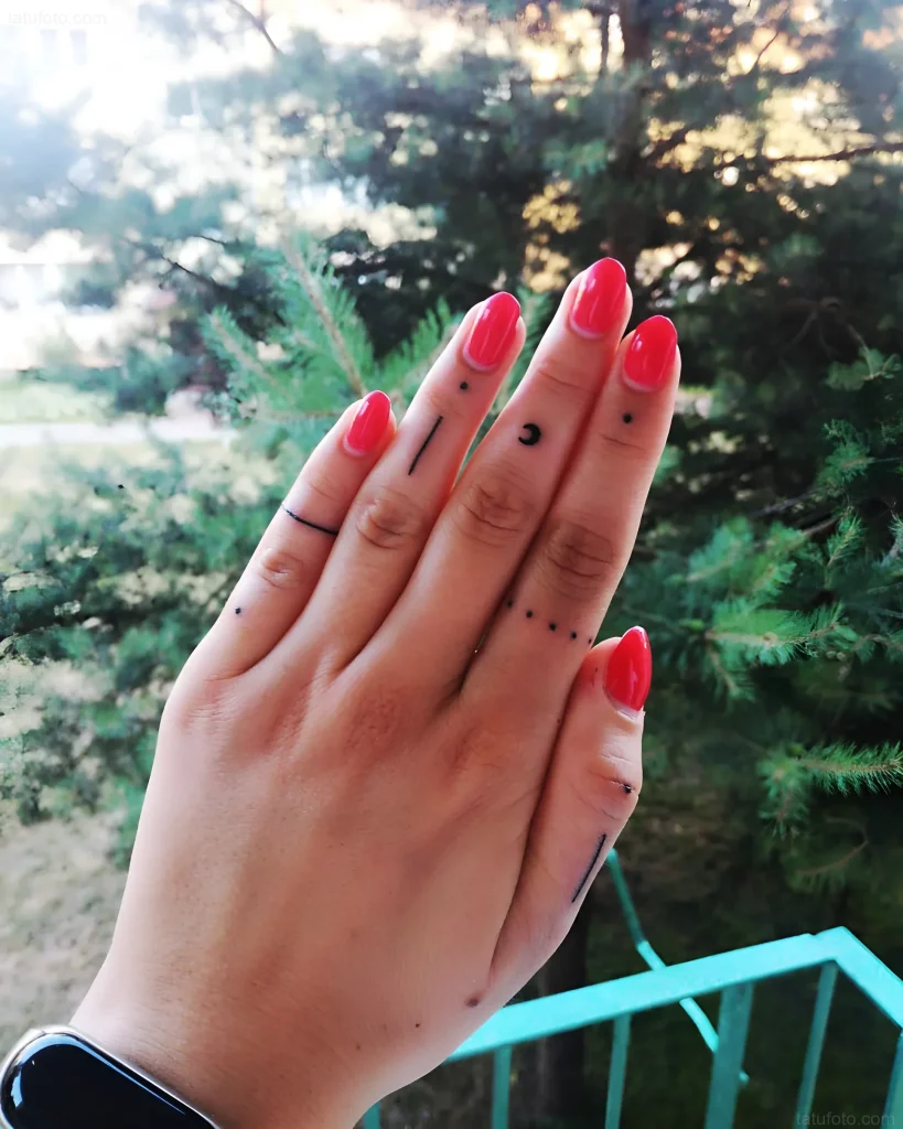 手指纹身照片:月相,垂直线条和圆点,黑色,在带红色美甲的女性手上。