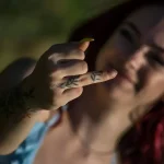 Фотография девушки с татуировкой в виде тонкой веточки с листьями, обвивающей палец. Минималистичный дизайн, акцент на детализацию.