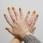 Фотография двух рук с минималистичными татуировками на пальцах: крест, стрела, лилия, ромб и точки.