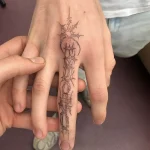 Черно-белая татуировка на пальце руки, выполненная в стиле Blackwork, с геометрической надписью и острыми элементами.