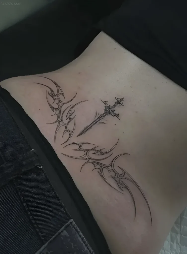Black and white lower back tattoo: a sword pierced by tribal patterns, symbolizing willpower and protection.