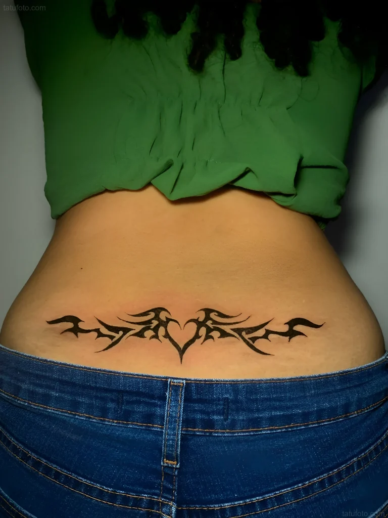 Black and white tribal tattoo on the lower back with a heart, done with clean lines.