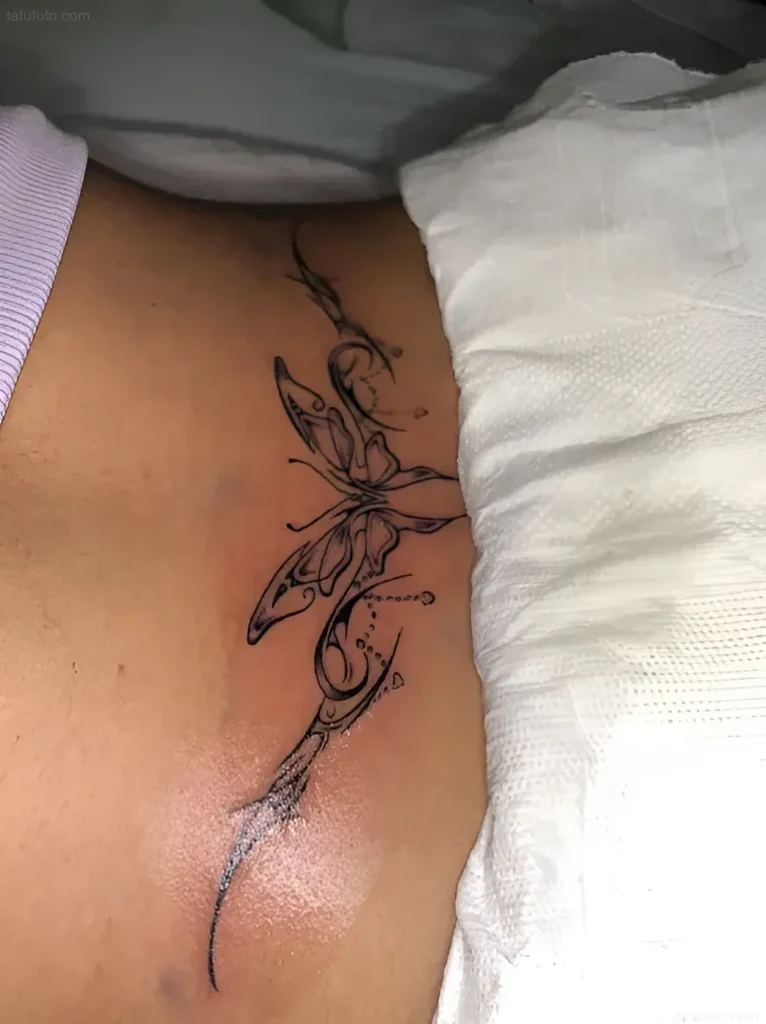 Black and white butterfly tattoo on a woman's lower back, done in a graphic style with tribal elements and thin lines.