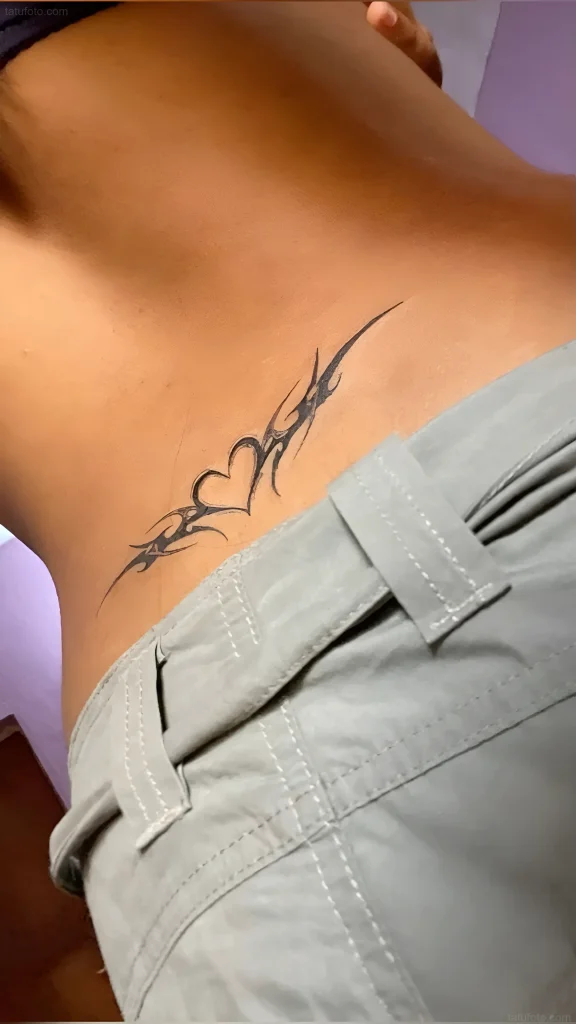 Photo of a lower back tattoo: black tribal pattern with a heart, done with clean lines.