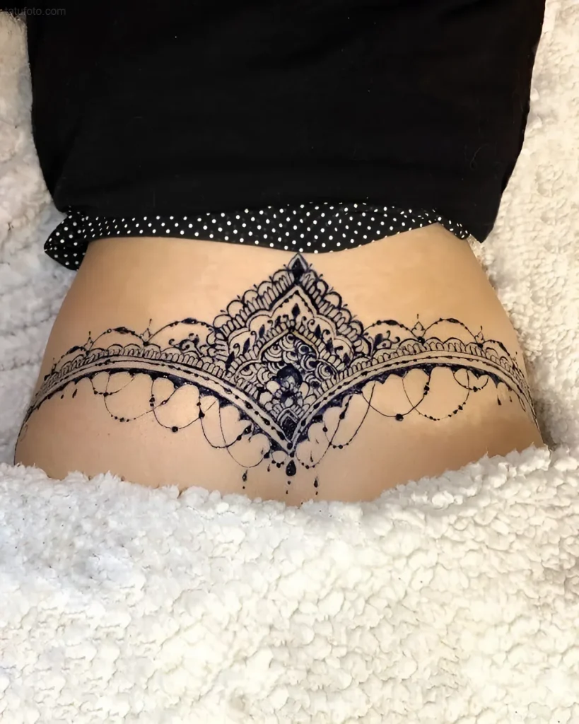 Black and white mandala tattoo on the lower back, done in fine line graphic technique, with emphasis on detail and symmetry.