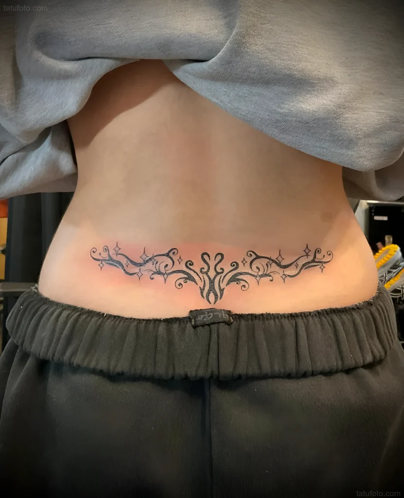 Black and white lower back tattoo with a floral pattern and small stars, done in a graphic style.