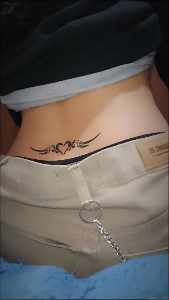 Photo of a lower back tattoo: black tribal-style weaving in the shape of a heart, on a woman's back.