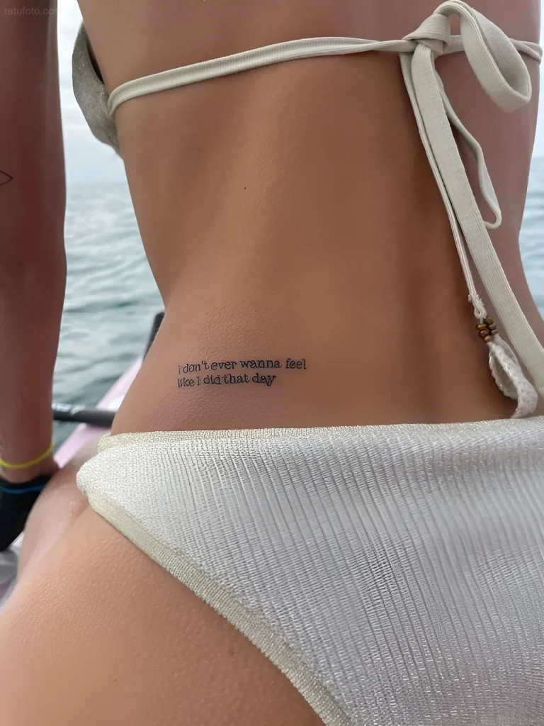 Photo of a lower back tattoo on a girl: black inscription 'I don't ever wanna feel like I did that day' along the spine.
