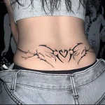 Черно-белая татуировка на пояснице девушки в стиле Tribal Heart с острыми шипами, обрамляющими сердце