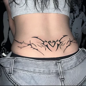 Черно-белая татуировка на пояснице девушки в стиле Tribal Heart с острыми шипами, обрамляющими сердце