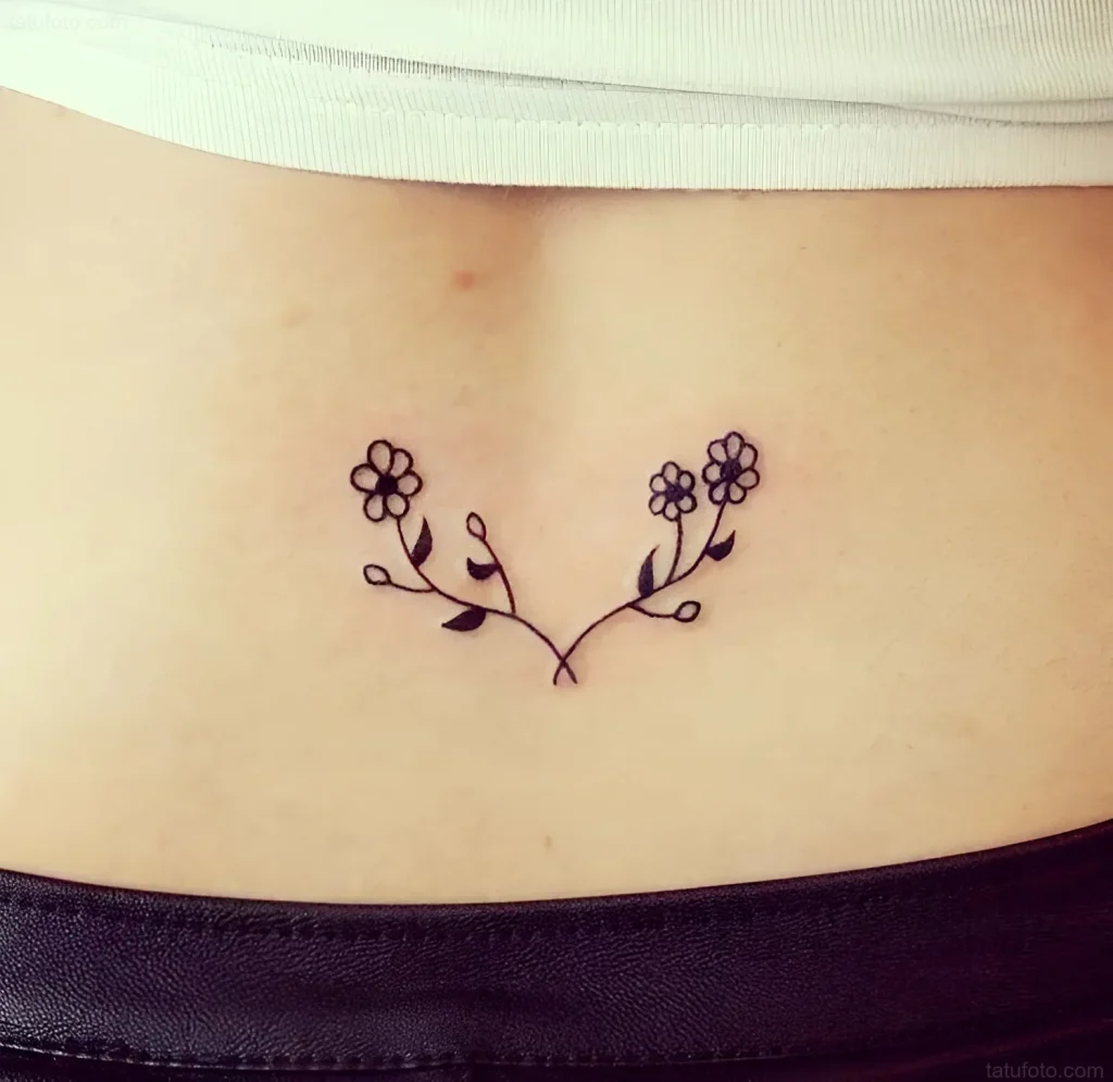 Photo of a lower back tattoo: a thin black branch with two groups of small flowers, done in a minimalist style.