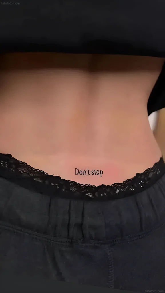 Photo of a lower back tattoo with the inscription 'Don't stop' in black, done in a minimalist font. Part of the hips and underwear is visible.