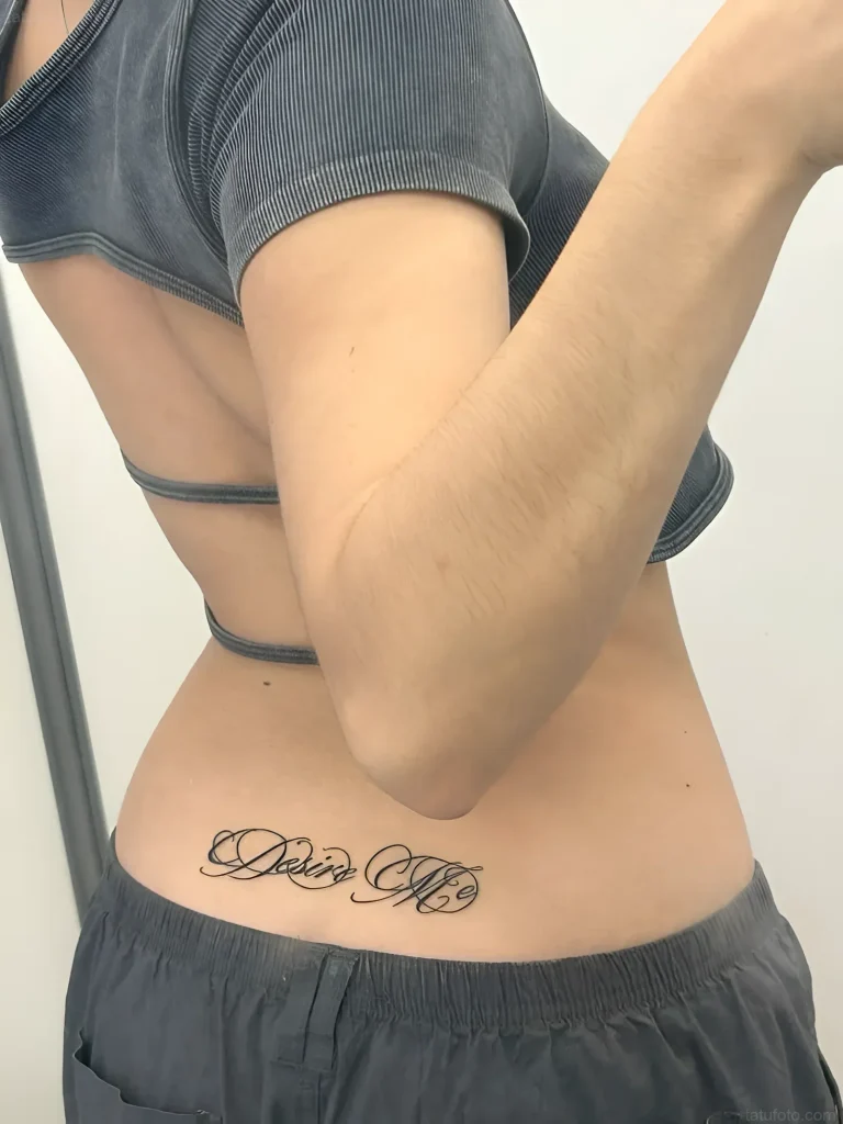 Photo of a tattoo: elegant calligraphic inscription 'Daisy Mae' on a girl's lower back, done in black ink.