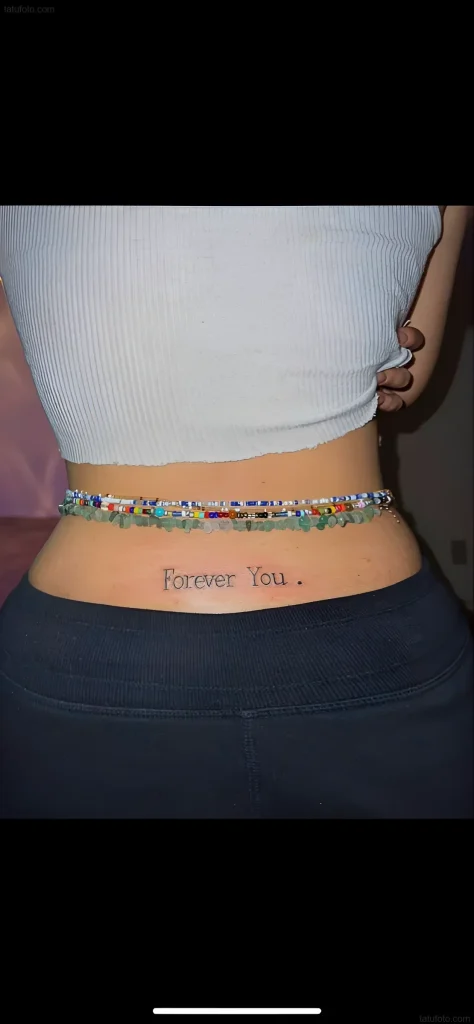 Photo of a lower back tattoo with the inscription 'Forever You' in a thin font, placed horizontally between the hips.