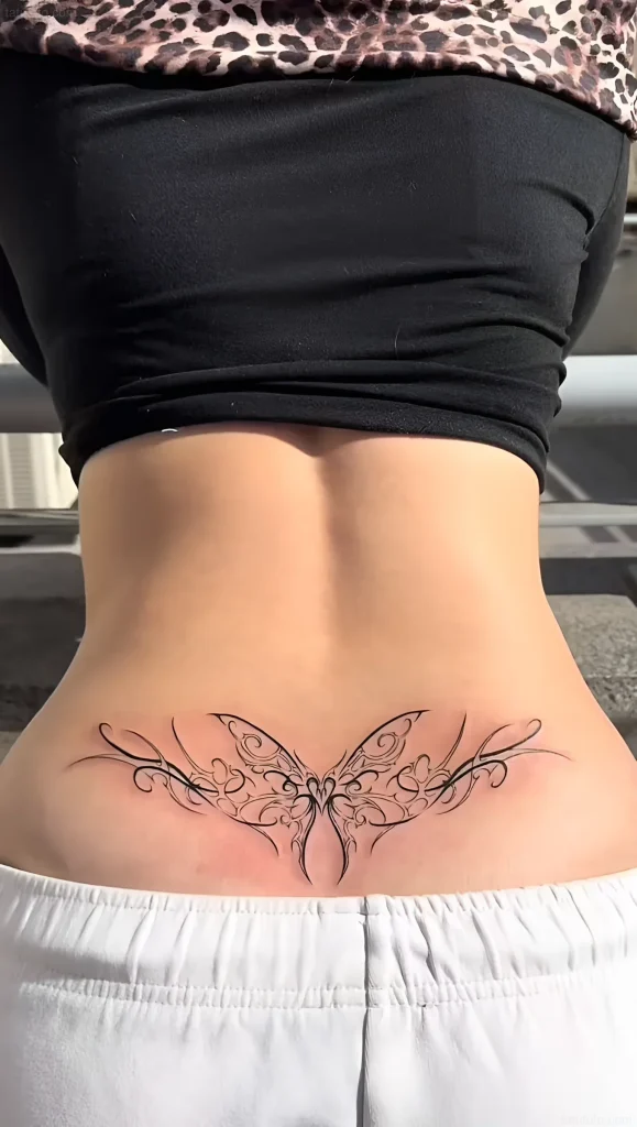 Photo of a butterfly tattoo on the lower back, done in a graphic style with smooth lines and emphasis on symmetry.