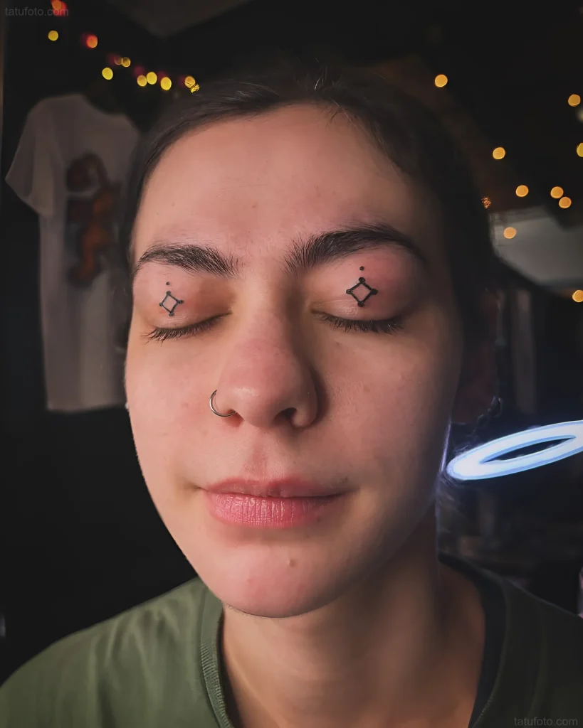 Photograph of a girl with closed eyes and minimalist geometric symbol tattoos on her eyelids, done in a micro-tattoo technique.