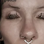 Черно-белая татуировка на веках с надписями 'Good' и 'Life' под ресницами, выполненная в стиле минимализм.