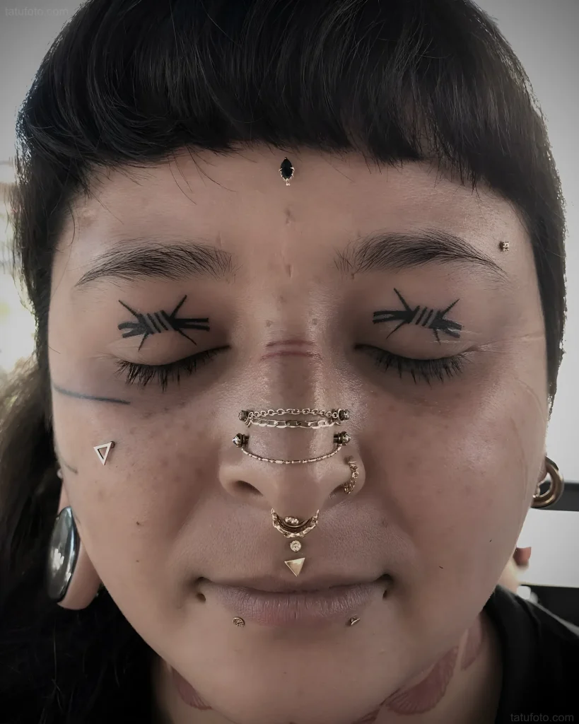 Photo of a girl with an eyelid tattoo mimicking closed eyes and multiple piercings on her face.