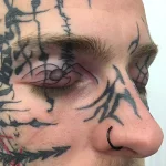 Фото татуировки: минималистичный паук с геометрическим узором на веке мужчины, выполненный в технике blackwork.