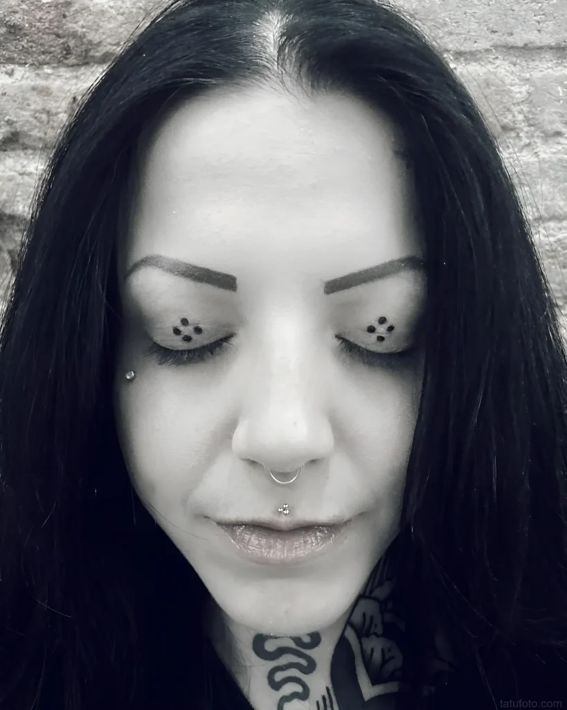 Black and white photo of a girl with a tattoo of several small dots under each eye, emphasizing the expressiveness of her gaze.