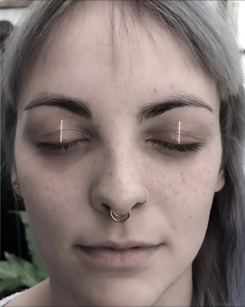 Photo of a tattoo: two thin white vertical lines on a girl's eyelids, minimalism, modern style.
