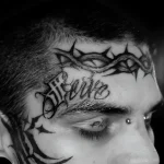 Черно-белая татуировка на веке с надписью 'Love' и терновым венцом, выполненная в стиле blackwork.