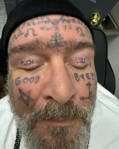 Фото татуировки на веках мужчины с надписями 'FUCK', 'GOOD', 'BYE' и 'YOU', а также символами и буквами на лбу.