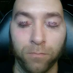 Мужчина с татуировкой «Game Over» на веках, выполненной в минималистичном стиле, крупный план.