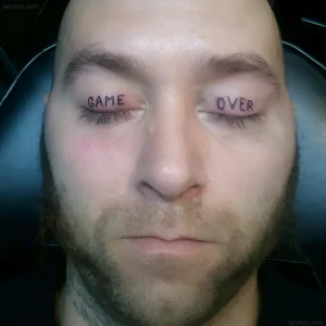 Мужчина с татуировкой «Game Over» на веках, выполненной в минималистичном стиле, крупный план.