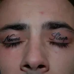 Чёрная татуировка надписью 'Never Sleep' на веках молодого человека, крупный план.