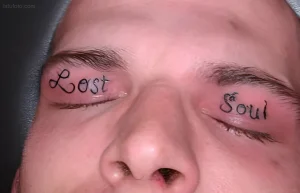 Фотография татуировки на веках с надписью «Lost Soul» - черные буквы, выполненные в минималистичном стиле, расположены под бровями.