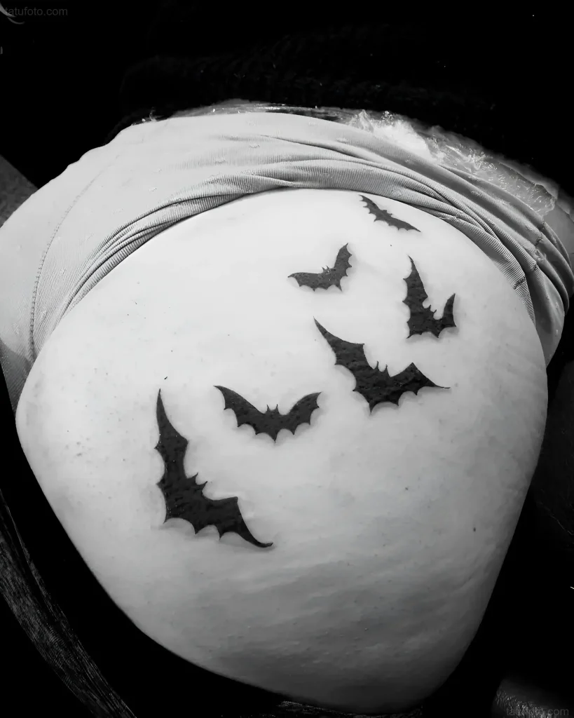 Black and white tattoo of bat silhouettes on the buttock, done in a minimalist style.