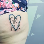 Фотография татуировки на ягодице: черная надпись 'GRL PWR' заключена в контур сердца, выполненная в минималистичном стиле.