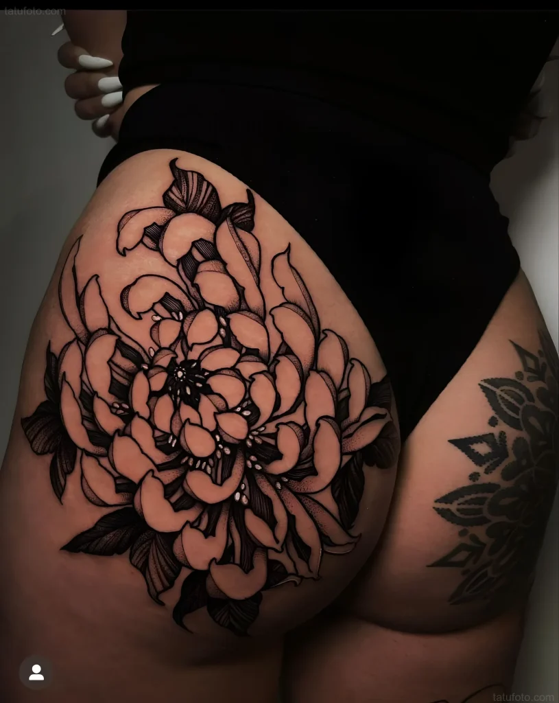 Black and white peony tattoo on the buttock, in a graphic style with detailed petals and leaves.