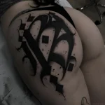 Черно-белая татуировка на ягодице, выполненная в стиле Blackwork, с абстрактным изображением буквы и геометрическими элементами.