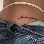 Фото татуировки на ягодицах: надпись 'love yourz' красными чернилами, выполненная каллиграфическим шрифтом на нижней части спины девушки.