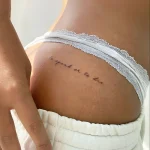 Фотография татуировки на ягодице: изящная надпись 'to speak or to die' черными чернилами, выполненная тонкой линией.