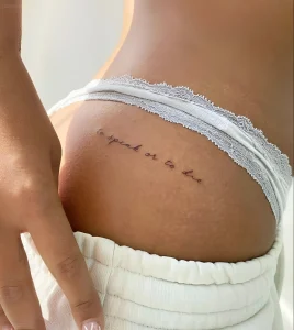 Фотография татуировки на ягодице: изящная надпись 'to speak or to die' черными чернилами, выполненная тонкой линией.