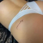 Минималистичная татуировка надписью 'peachy' на коже ягодицы, выполненная тонкой линией.